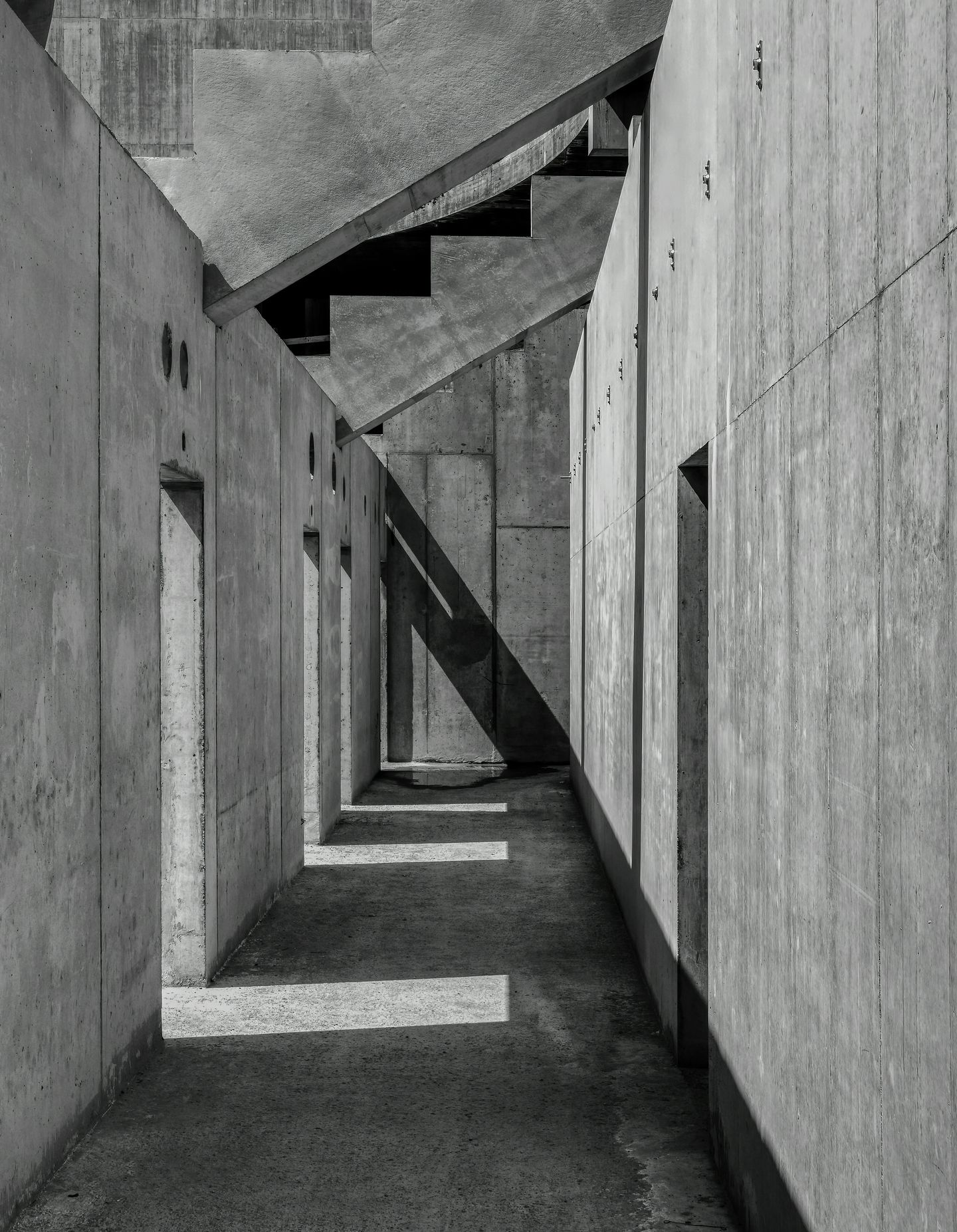 Schmaler Gang aus Beton mit Treppen und Lichtstreifen